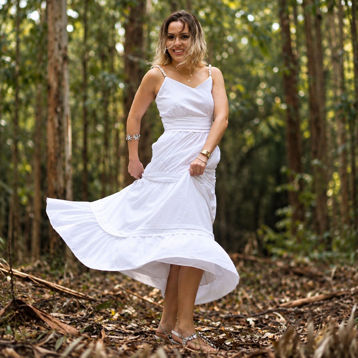 Denise em um cenário arborizado, com vestido branco